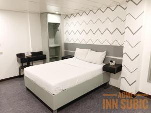 1 dormitorio con 1 cama blanca y 2 mesas en ACME Inn Subic, en Olóngapo