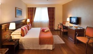 a hotel room with a bed and a desk and a television at Hotel Calissano in Alba