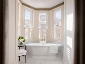 a white bath tub in a bathroom with windows at Kimpton - Fitzroy London, an IHG Hotel in London