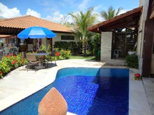 ein Pool mit Tisch und Sonnenschirm neben einem Haus in der Unterkunft BANGALÔ PRAIA DE MURO ALTO/PORTO DE GALINHAS in Porto De Galinhas