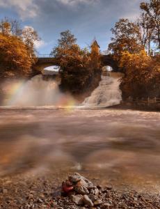 a river with a waterfall and a bridge with a rainbow at Villa du Lac de Coo in Stavelot