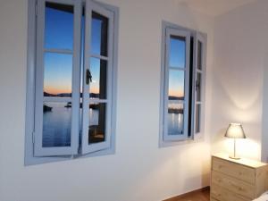 a bedroom with two windows and a lamp on a dresser at Aegina Port Apt 2-Διαμέρισμα στο λιμάνι της Αίγινας 2 in Egina