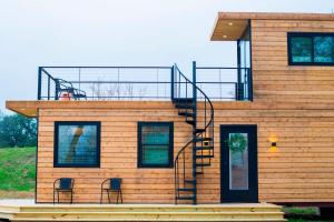 Cool River "Helm" Container Home في Bellmead: منزل خشبي مع درج وكرسيين