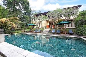a swimming pool with chairs and umbrellas next to a house at Bhanuswari Villas Ubud in Ubud
