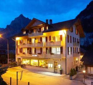Un grand bâtiment blanc avec des lumières la nuit dans l'établissement Hotel Des Alpes, à Kandersteg