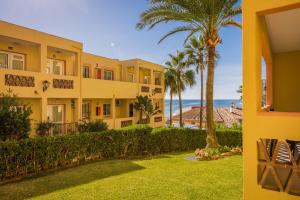 a yellow building with a palm tree and the ocean at Macdonald Doña Lola Resort in La Cala de Mijas