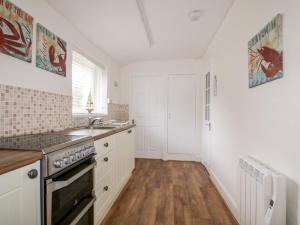 Una cocina con gabinetes blancos, un fregadero y una estufa. en Cove Cottage, en Tintagel
