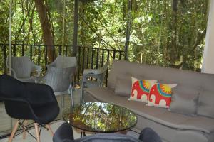 a porch with a couch and chairs and trees at Shadow Grove Camping & Cabins Kitulgala in Kitulgala