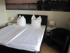 a bed with white sheets and a black chair at Pension Sonnengrund in Nonnenhorn