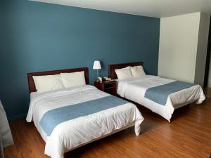 two beds in a room with blue walls and wooden floors at Motel Le Rond Point in Metabetchouan