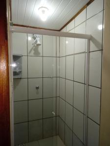 La salle de bains est pourvue d'une douche et de murs carrelés blancs. dans l'établissement Pousada Vento & Cia, à Farol de Santa Marta