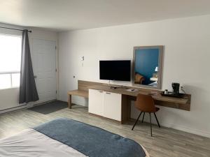 a bedroom with a bed and a desk with a television at Motel Le Rond Point in Metabetchouan