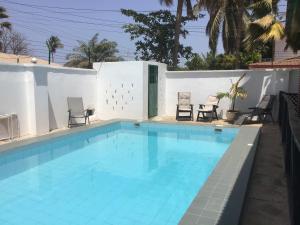 a swimming pool with chairs next to a white wall at Anns Guesthouse BakauGambia in Bakau