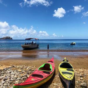 two kayaks on a beach with a boat in the water at Soufriere Guesthouse in Soufrière
