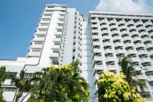 a tall white building with palm trees in front of it at Grand Jomtien Palace Hotel - SHA Extra Plus in Jomtien Beach