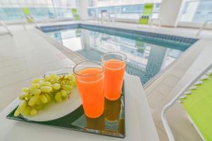due bicchieri di succo d'arancia e uva su un vassoio accanto alla piscina di VISTA HOTEL APARTMENTS DELUXE a Dubai