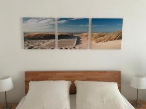 four paintings of a beach and a boardwalk in a bedroom at Steiner Strandappartements Appartement 208 Süd- Landseite in Stein