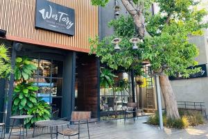 una cafetería con mesas y sillas frente a un edificio en Westory Design Poshtel en Kanchanaburi