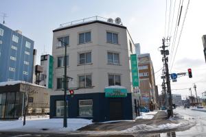 a tall white building on a city street with snow at Economy Hotel Upashi in Asahikawa