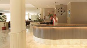 a man standing behind a counter in a lobby with a clock at Garbi Cala Millor in Cala Millor +22 photos
