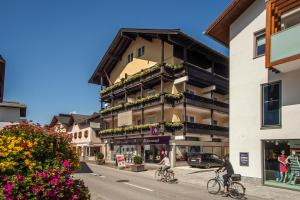 duas pessoas a andar de bicicleta numa rua em frente a um edifício em Panoramahotel em Sankt Johann in Tirol