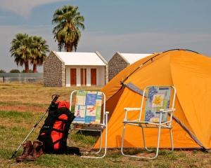 una tienda naranja y dos sillas en un campo en Kalahari Farmhouse Campsite, en Stampriet