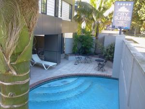 a swimming pool next to a building with a palm tree at City Suites in Tauranga