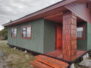une petite maison verte avec une terrasse couverte en bois dans l'établissement Cabañas Troncos de Alerce en Puerto Montt con tinaja caliente, à Alerce