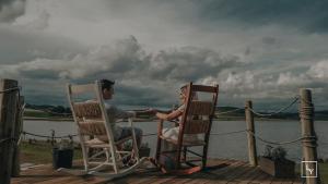 a man and woman sitting in rocking chairs on a dock at Tedesco Eco Park in São Francisco de Paula
