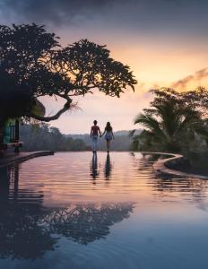 a couple standing in the water in front of the sunset at Adiwana Dara Ayu Villas in Payangan