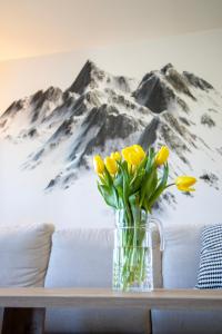 a vase of yellow flowers on a table with a mountain mural at Apartmán Háje - V srdci Tatier in Starý Smokovec