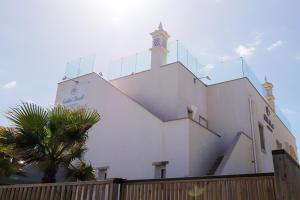 een wit gebouw met een klokkentoren en een palmboom bij Golden Beach Guest House & Rooftop Bar in Faro