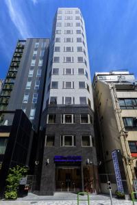 een hoog wit gebouw voor twee hoge gebouwen bij Shinbashi Urban Hotel in Tokyo
