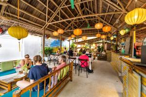 a group of people sitting at tables in a restaurant at Under The Coconut Tree Hoi An Homestay in Hoi An