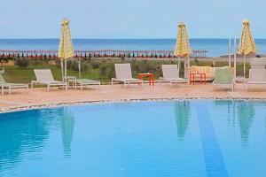 a swimming pool with chairs and umbrellas and the ocean at Litohoro Olympus Resort Villas & Spa in Plaka Litochorou +82 photos