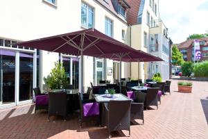an outdoor patio with tables and chairs and an umbrella at ACHAT Hotel Buchholz Hamburg in Buchholz in der Nordheide