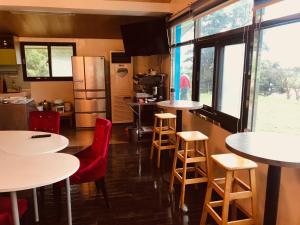 una cocina con mesas blancas, sillas rojas y ventanas en 睡海邊-小木屋, en Suao