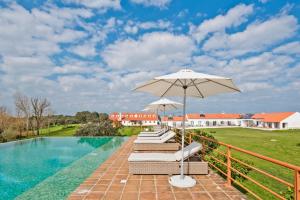 a group of lounge chairs with an umbrella next to a pool at Herdade do Barrocal de Baixo in Montemor-o-Novo