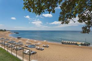 ein Strand mit Sonnenschirmen und Liegestühlen und dem Meer in der Unterkunft Troas Beach Hotel in Tavaklı