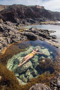 a woman floating in a pool of water on a rocky beach at Casa Calma Yoga Guesthouse in Agaete