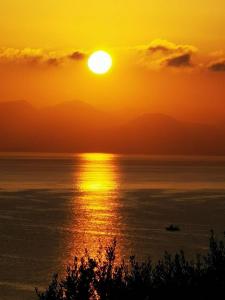 a sunset over the ocean with a boat in the water at Nikoli Apartments in Benitses