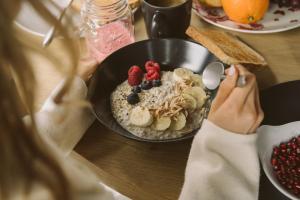 a woman sitting at a table with a bowl of oatmeal with fruit on it at The HEY HOTEL in Interlaken
