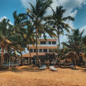 a building on a beach with palm trees and chairs at Jasmine Garden Beach Guest House in Hikkaduwa
