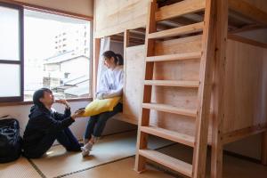 a man and a woman sitting on the floor next to a bunk bed at Fukuoka Guesthouse SHIP in Fukuoka