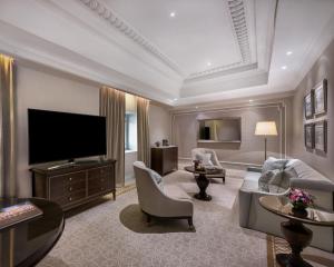 a living room with a television and a couch and chairs at The Fullerton Hotel Singapore in Singapore