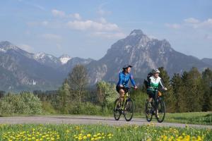 two people riding bikes down a road with mountains in the background at Haus Bagci in Füssen