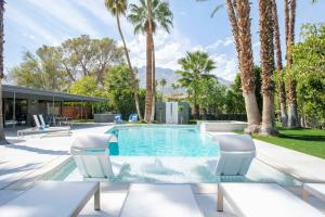 a swimming pool with two chairs and palm trees at Villa Perfetto Plaza in Palm Springs