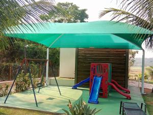a playground with a green umbrella and a swing at Aldeia do Lago C405-churrasqueira, bebidas liberadas nas piscinas, internet no ap, rampa de acesso ao lago, recarga carro elétrico, pesqueiro in Caldas Novas