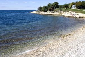 a beach with people sitting on the shore of the water at Hotel Albatros Plava Laguna in Poreč