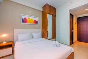 a bedroom with a large white bed with two shoes on it at Homey and Relaxing Studio @ Grand Dhika City Apartment By Travelio in Padurenan +6 photos